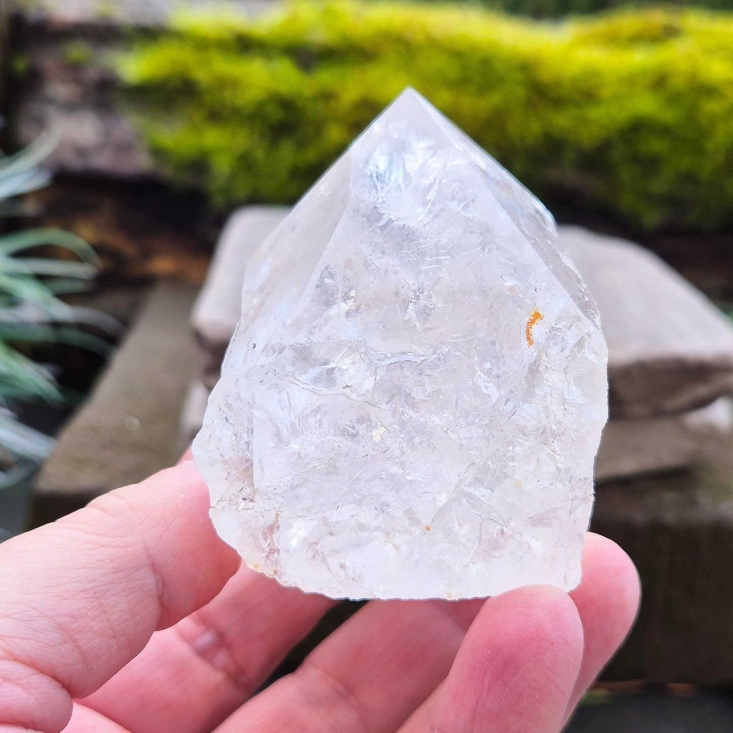 Quartz Crystal Standing Point from Brazil. This piece features a polished tip with a visible rainbow inclusion, contrasted by natural sides. The flat base allows it to stand freely, making it an ideal display crystal. It has lovely clarity, and the way it catches the light adds a beautiful reflective quality.