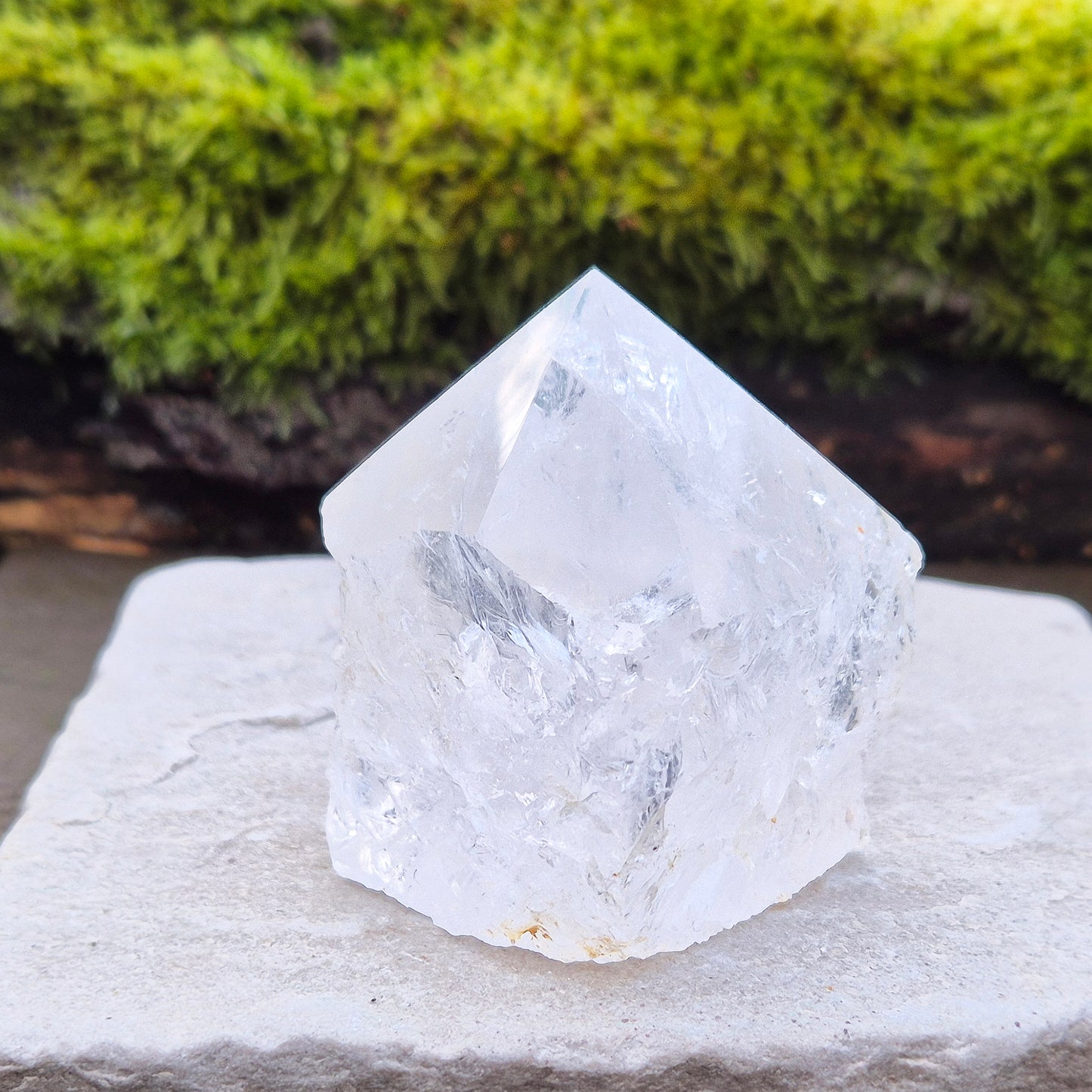 Quartz Crystal Standing Point from Brazil. This piece features a polished tip with a visible rainbow inclusion, contrasted by natural sides. The flat base allows it to stand freely, making it an ideal display crystal. It has lovely clarity, and the way it catches the light adds a beautiful reflective quality.