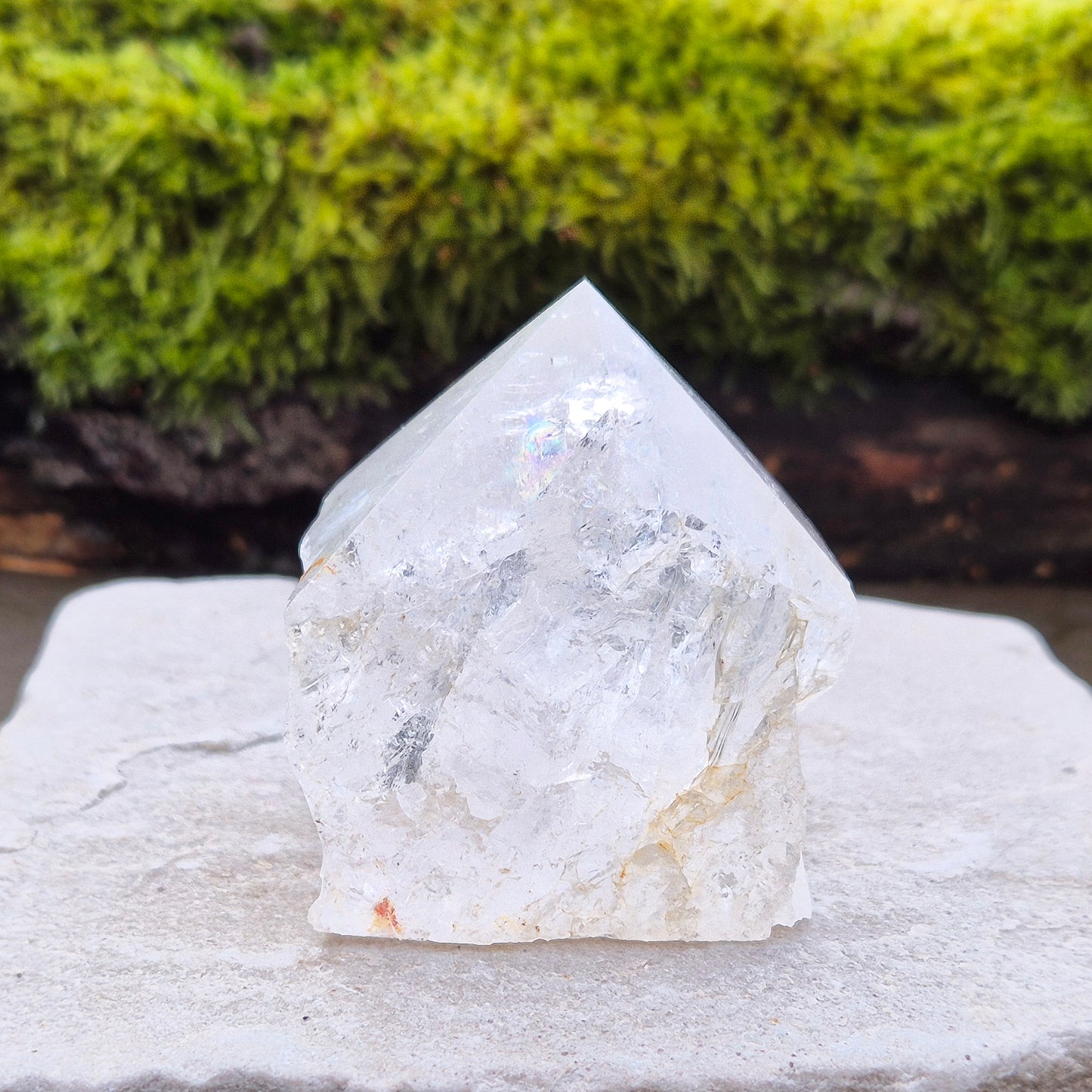 Quartz Crystal Standing Point from Brazil. This piece features a polished tip with a visible rainbow inclusion, contrasted by natural sides. The flat base allows it to stand freely, making it an ideal display crystal. It has lovely clarity, and the way it catches the light adds a beautiful reflective quality.