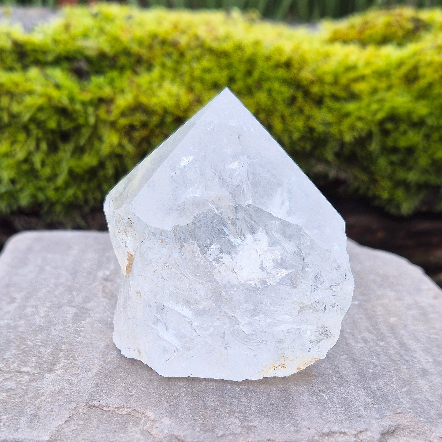 Quartz Crystal Standing Point from Brazil. This piece features a polished tip with a visible rainbow inclusion, contrasted by natural sides. The flat base allows it to stand freely, making it an ideal display crystal. It has lovely clarity, and the way it catches the light adds a beautiful reflective quality.