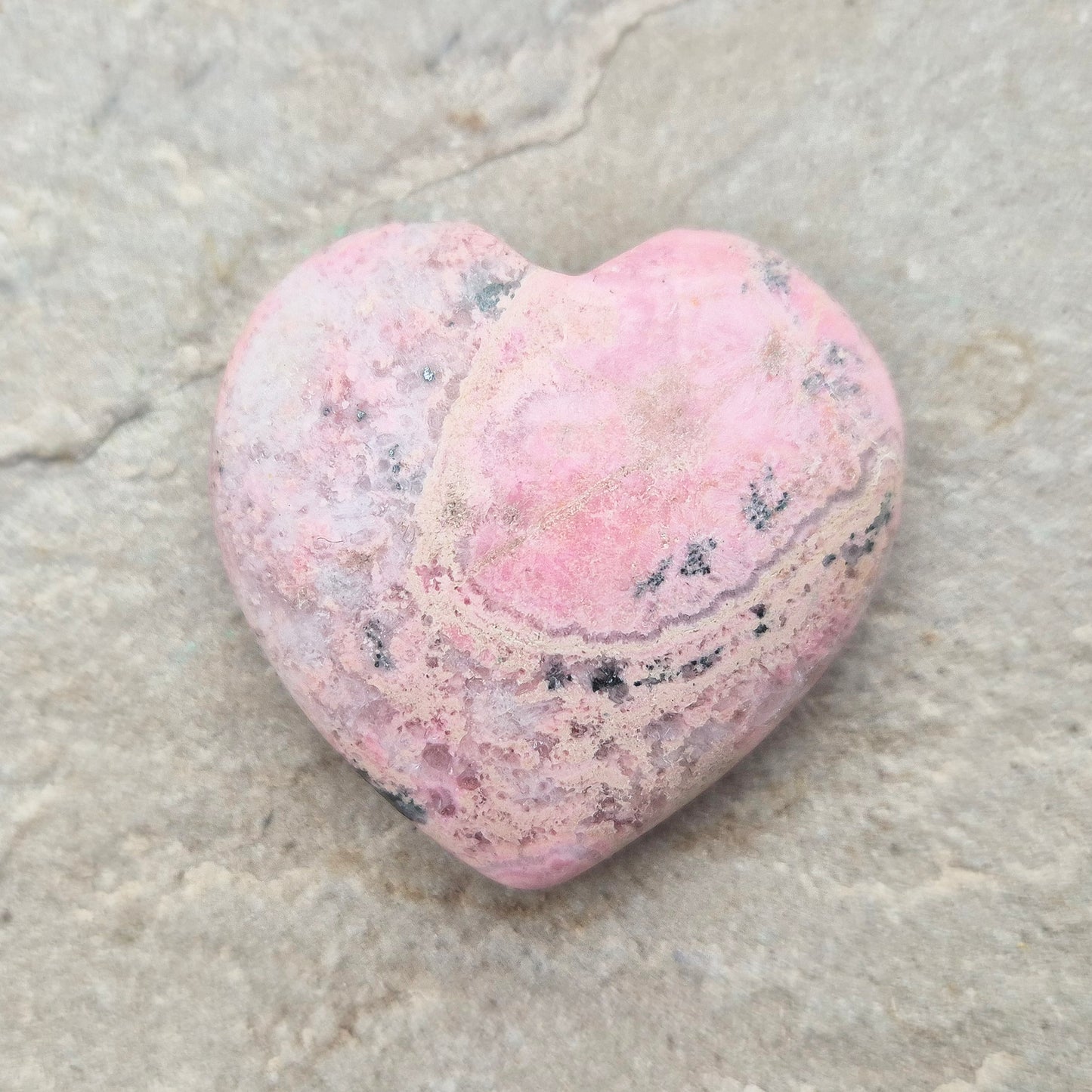 Pink Rhodonite Crystal Heart – also known as Bubblegum Pink Rhodonite from Peru. This beautiful heart-shaped Rhodonite crystal, sometimes nicknamed Bubblegum Pink Rhodonite, comes from Peru and features a soft pink colour with black patches caused by the natural oxidation of manganese.