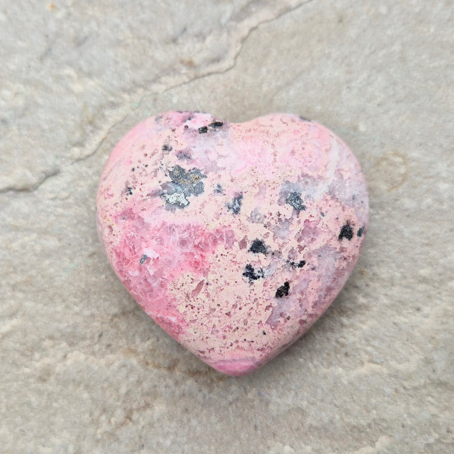 Pink Rhodonite Crystal Heart – also known as Bubblegum Pink Rhodonite from Peru. This beautiful heart-shaped Rhodonite crystal, sometimes nicknamed Bubblegum Pink Rhodonite, comes from Peru and features a soft pink colour with black patches caused by the natural oxidation of manganese.