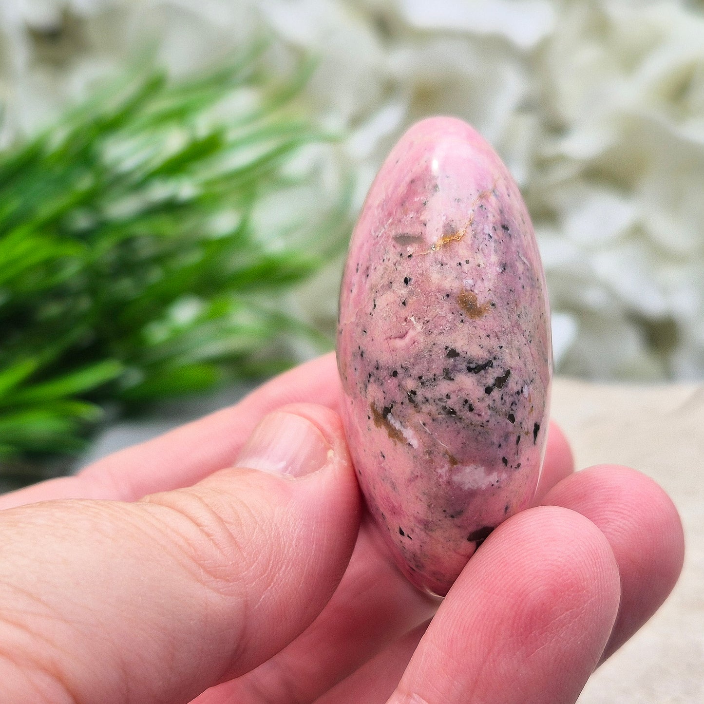 Pink Rhodonite Crystal Palm Stone – also known as Bubblegum Pink Rhodonite from Peru. This beautiful Rhodonite crystal, sometimes nicknamed Bubblegum Pink Rhodonite, comes from Peru and features a soft pink colour with black patches caused by the natural oxidation of manganese.