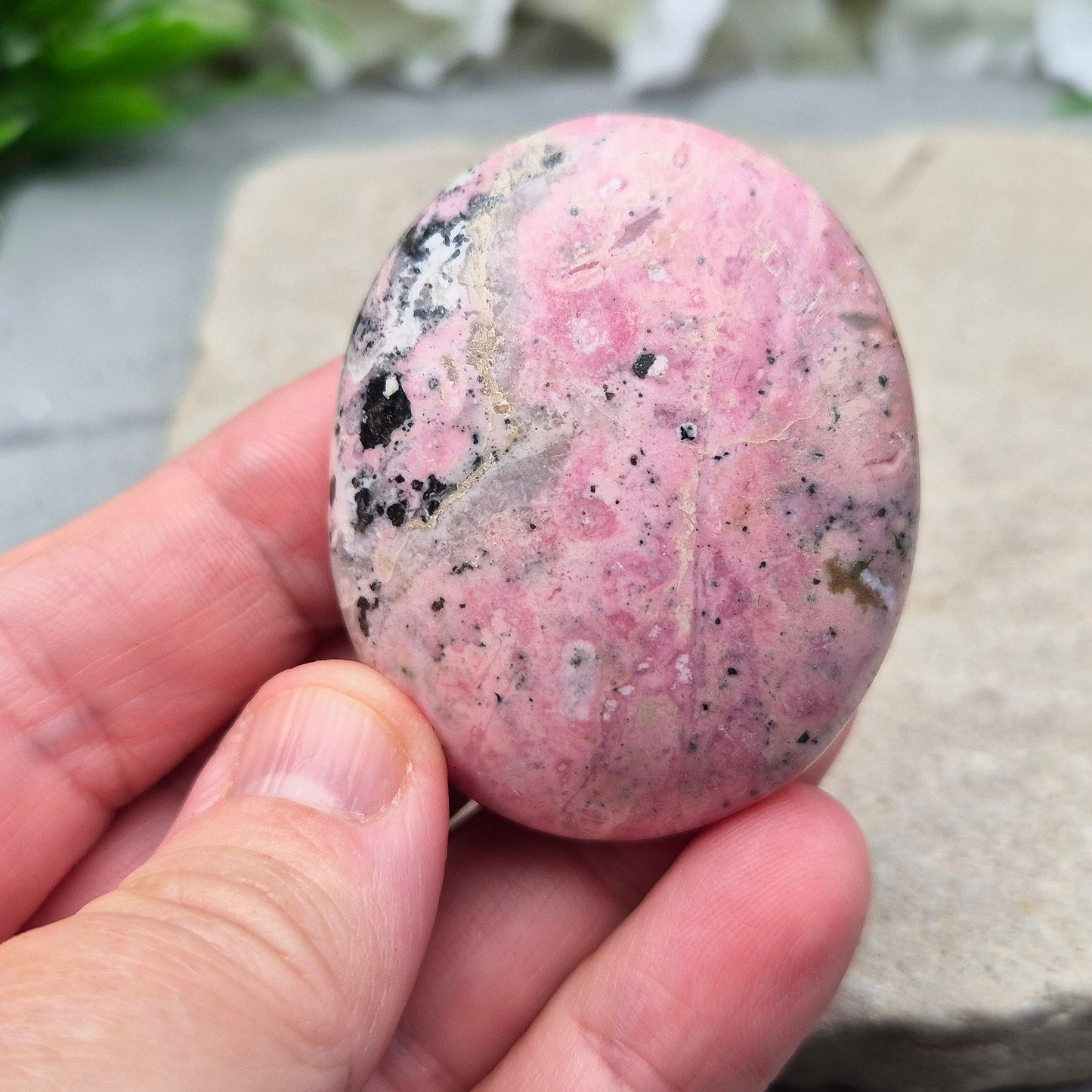 Pink Rhodonite Crystal Palm Stone – also known as Bubblegum Pink Rhodonite from Peru. This beautiful Rhodonite crystal, sometimes nicknamed Bubblegum Pink Rhodonite, comes from Peru and features a soft pink colour with black patches caused by the natural oxidation of manganese.