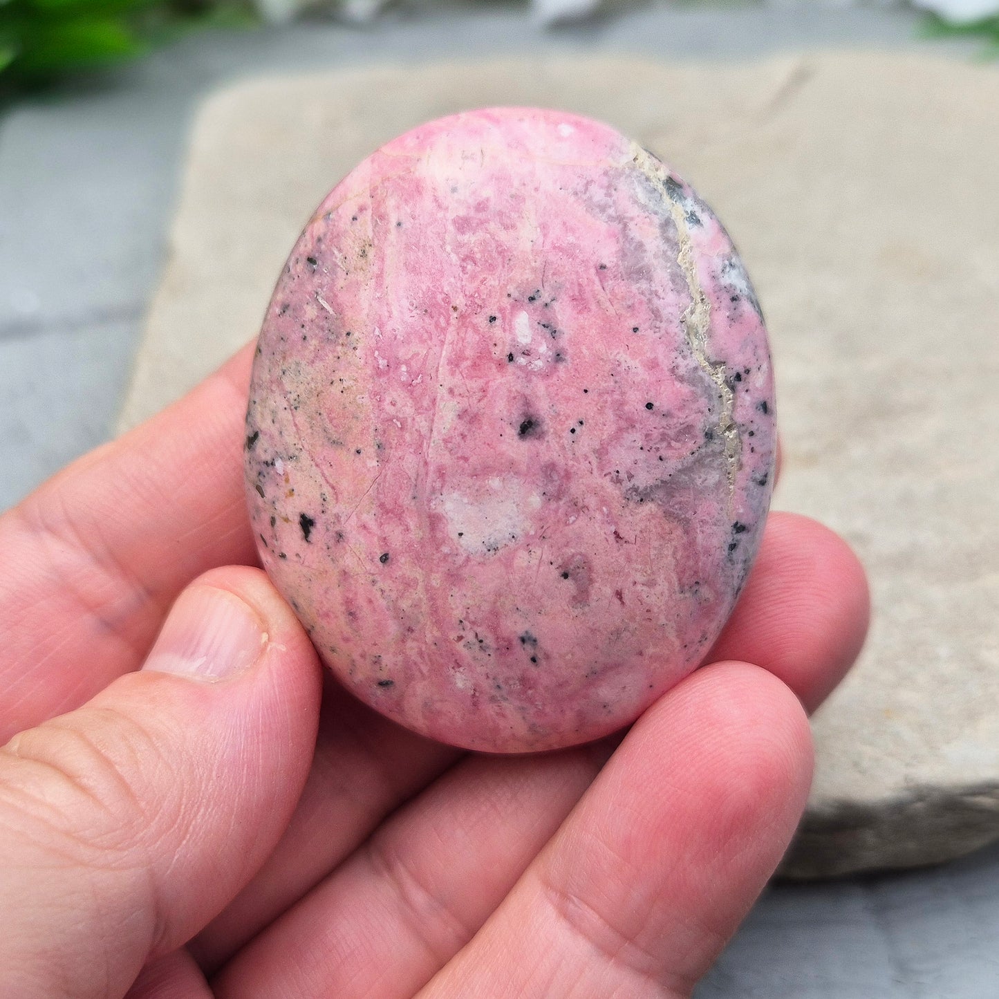 Pink Rhodonite Crystal Palm Stone – also known as Bubblegum Pink Rhodonite from Peru. This beautiful Rhodonite crystal, sometimes nicknamed Bubblegum Pink Rhodonite, comes from Peru and features a soft pink colour with black patches caused by the natural oxidation of manganese.