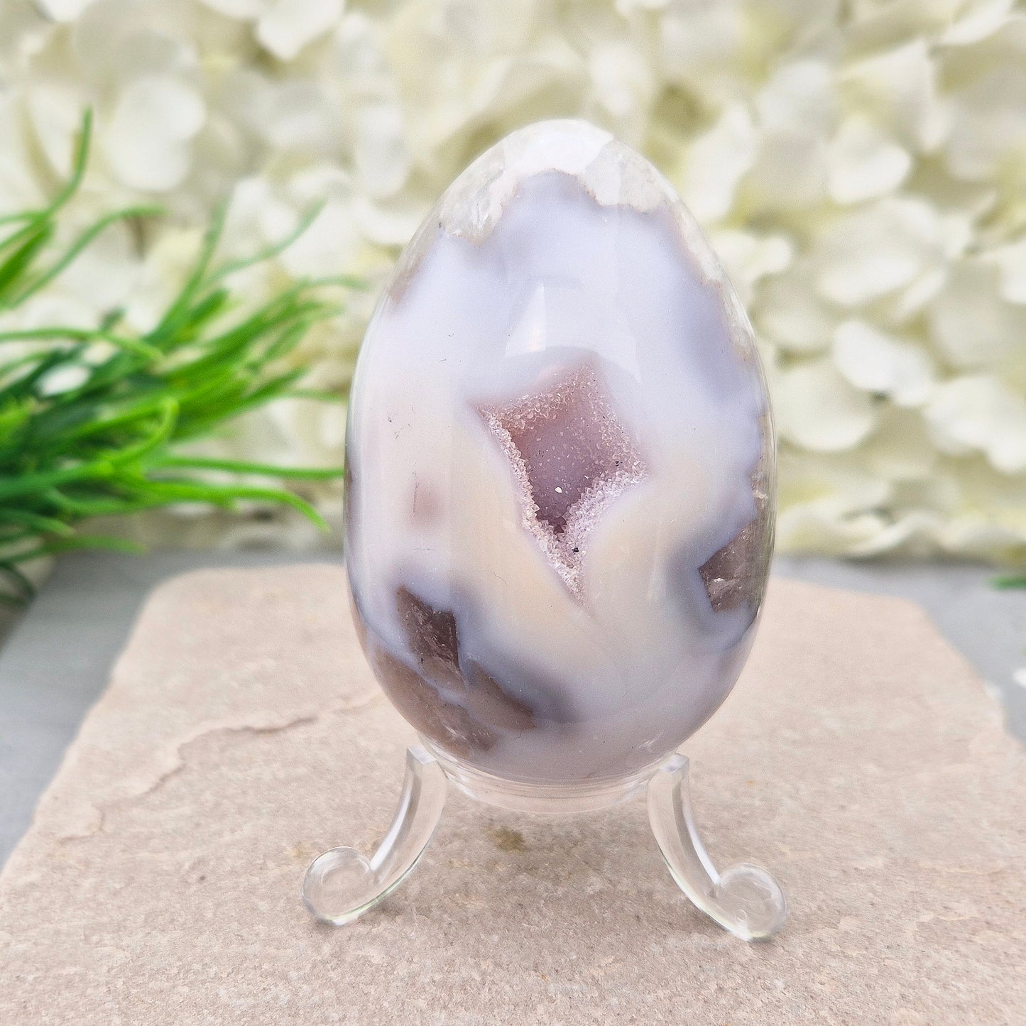 This beautiful Druzy Agate egg from Brazil is polished and showcases a sparkling pocket of natural druzy crystals in the middle of it. It comes with a clear acrylic stand, making it a lovely addition to any space or crystal shelf.