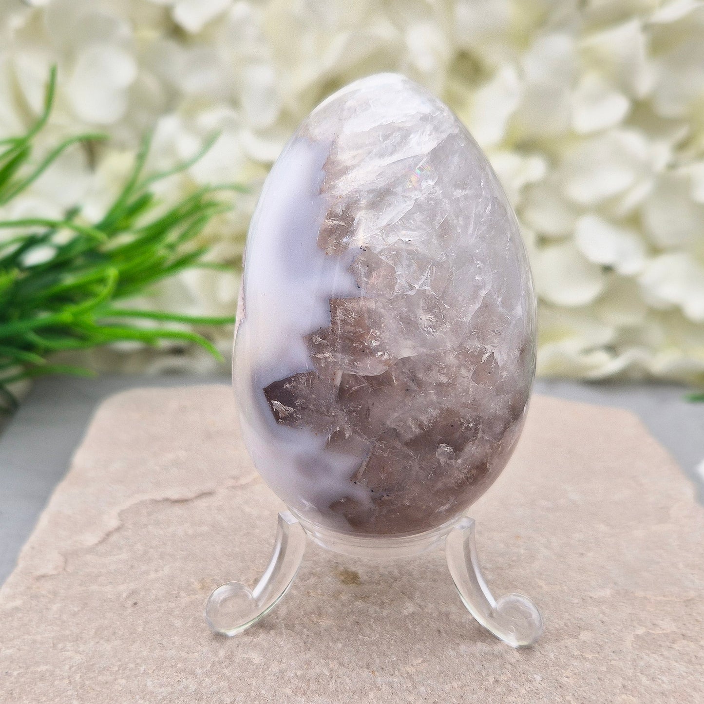 This beautiful Druzy Agate egg from Brazil is polished and showcases a sparkling pocket of natural druzy crystals in the middle of it. It comes with a clear acrylic stand, making it a lovely addition to any space or crystal shelf.