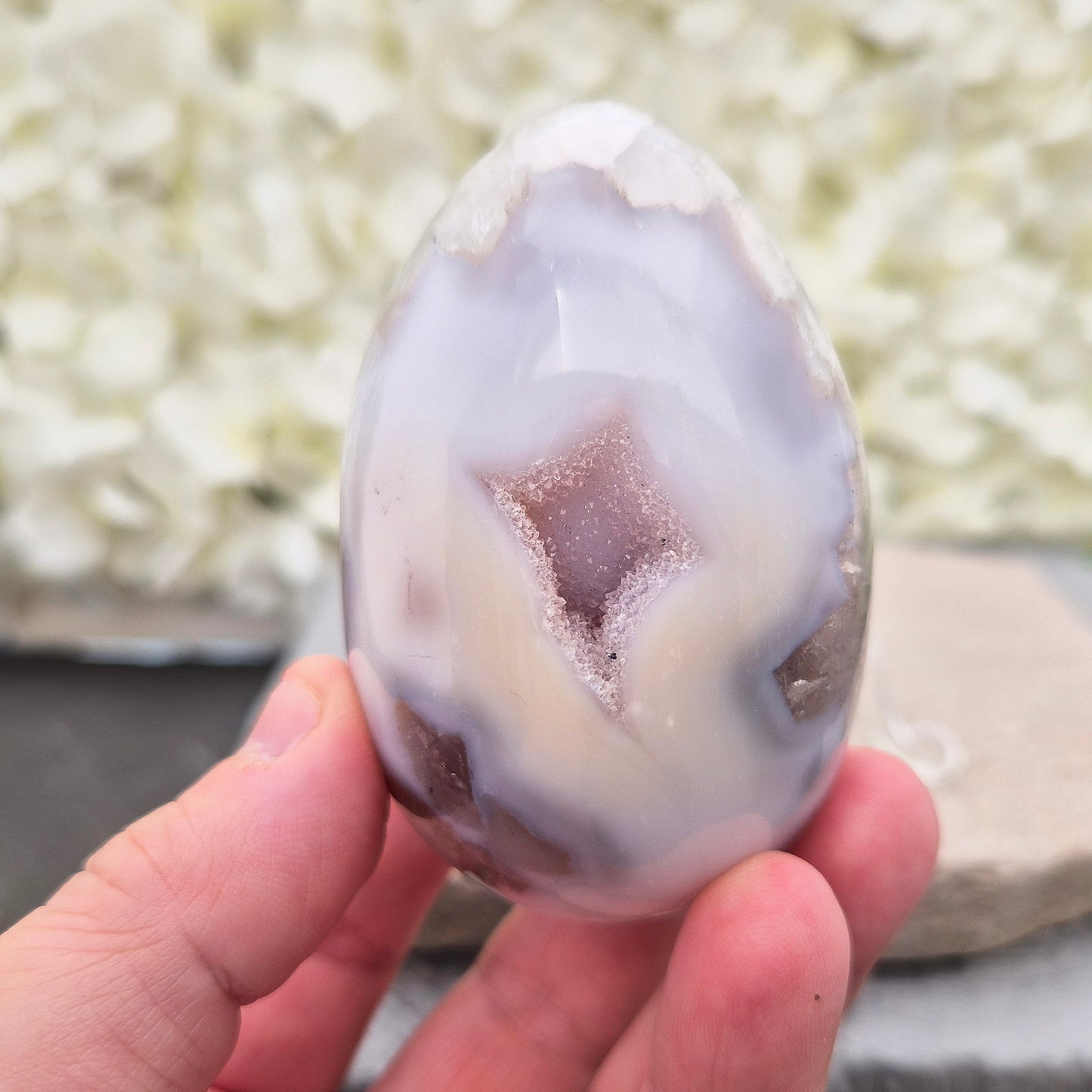 This beautiful Druzy Agate egg from Brazil is polished and showcases a sparkling pocket of natural druzy crystals in the middle of it. It comes with a clear acrylic stand, making it a lovely addition to any space or crystal shelf.