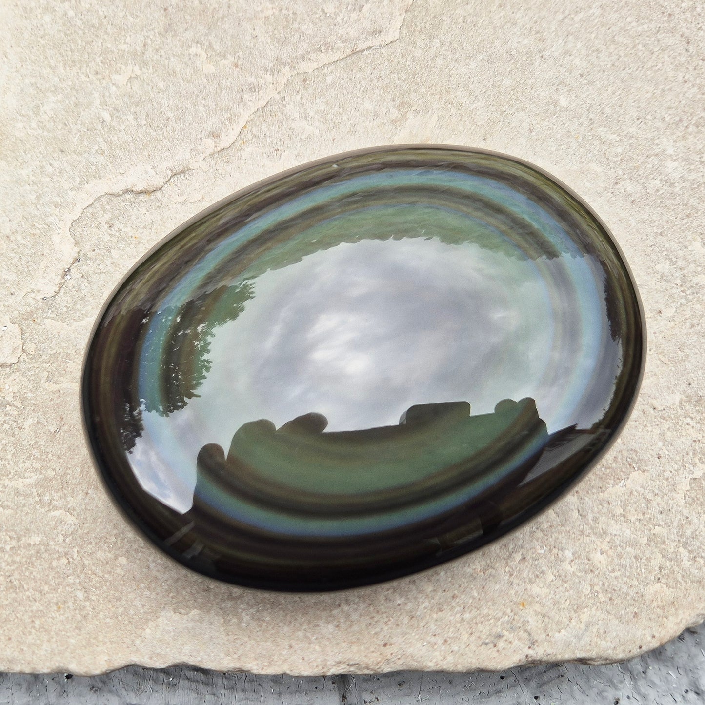 This highly polished, generously sized Rainbow Obsidian palmstone from Mexico reveals bands of deep green, gold, and shadowy blue — colours that only appear when the light hits just right.