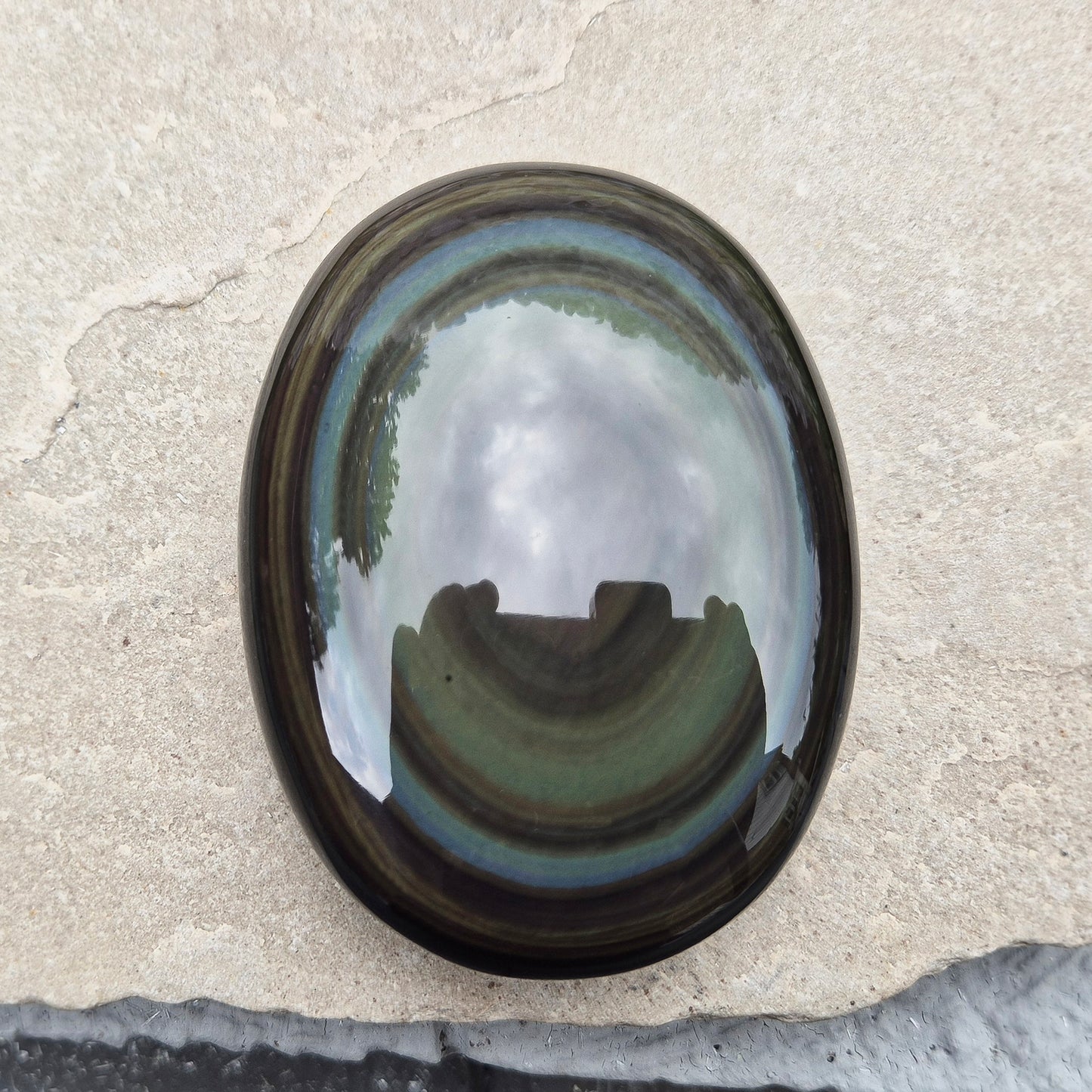 This highly polished, generously sized Rainbow Obsidian palmstone from Mexico reveals bands of deep green, gold, and shadowy blue — colours that only appear when the light hits just right.