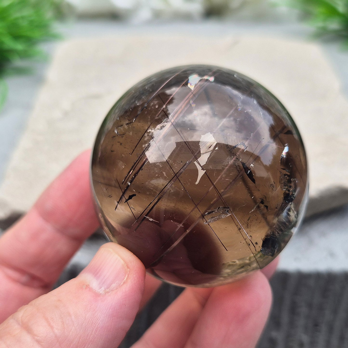 Smoky Quartz Sphere with Copper Red Rutile and rainbow flashes — grounding, protecting, and boosting creativity and clarity. Includes acrylic stand.