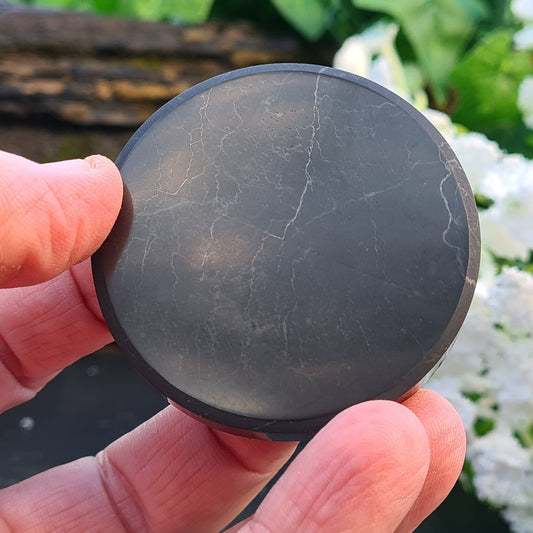 Shungite Disc from the Karelia region of Russia, polished to a smooth finish. Formed from rare carbon minerals over 2 billion years ago, it contains nearly all the minerals in the periodic table. Cleanse regularly and recharge in the sun. Can also be used as a platform for placing objects onto.