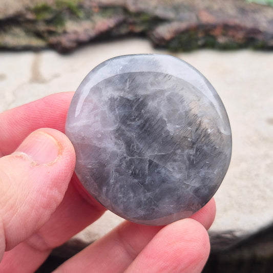 Lunar Quartz Crystal Palm Stone, also known as Lunar Rose Quartz, comes from Namibia. It is a blend of Rose Quartz and Graphite, creating unique color variations ranging from light grey to darker shades with pink hues.