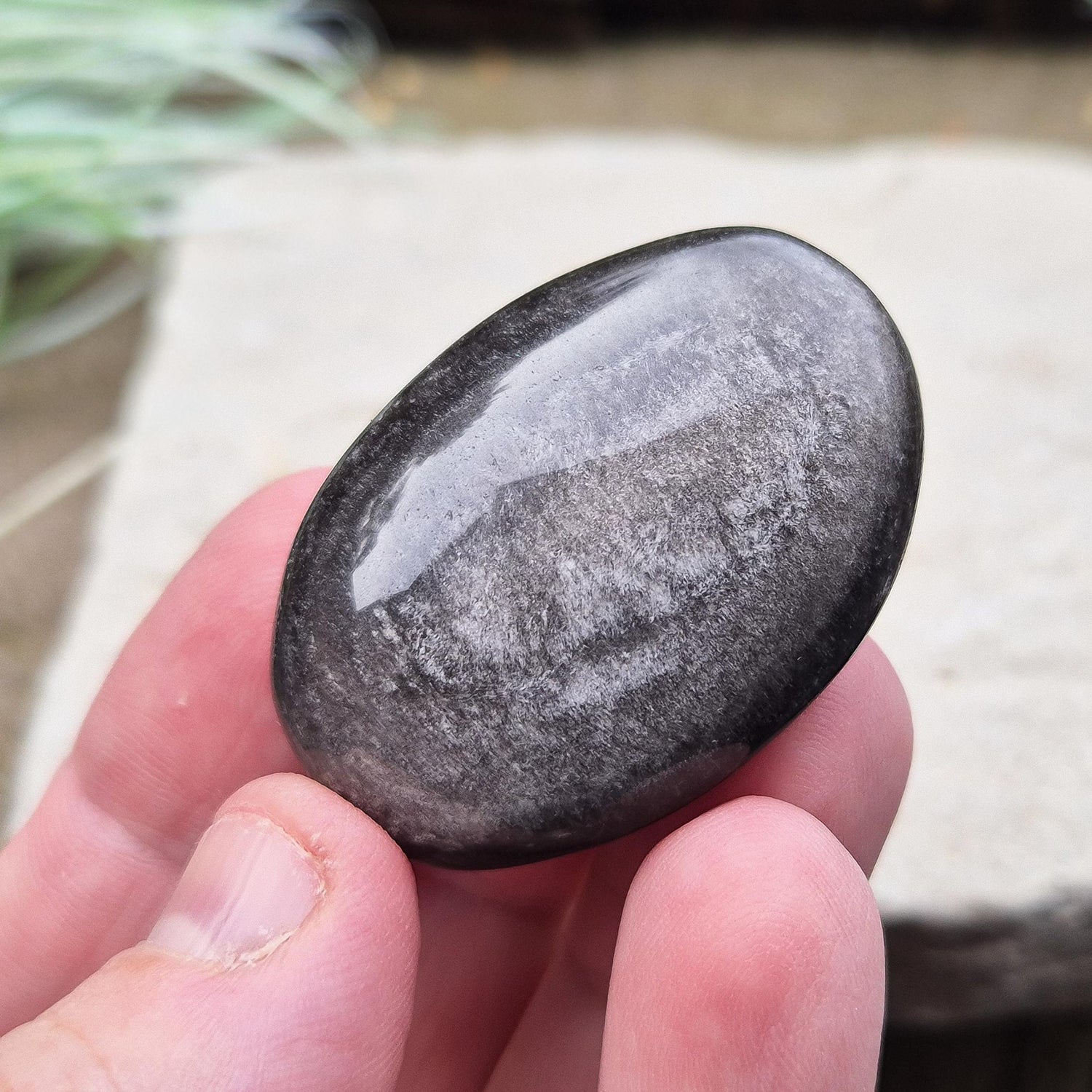 Silver Sheen Obsidian Palm Stone is a volcanic glass with a striking silvery or metallic sheen, created by tiny gas bubbles trapped during rapid lava cooling. 