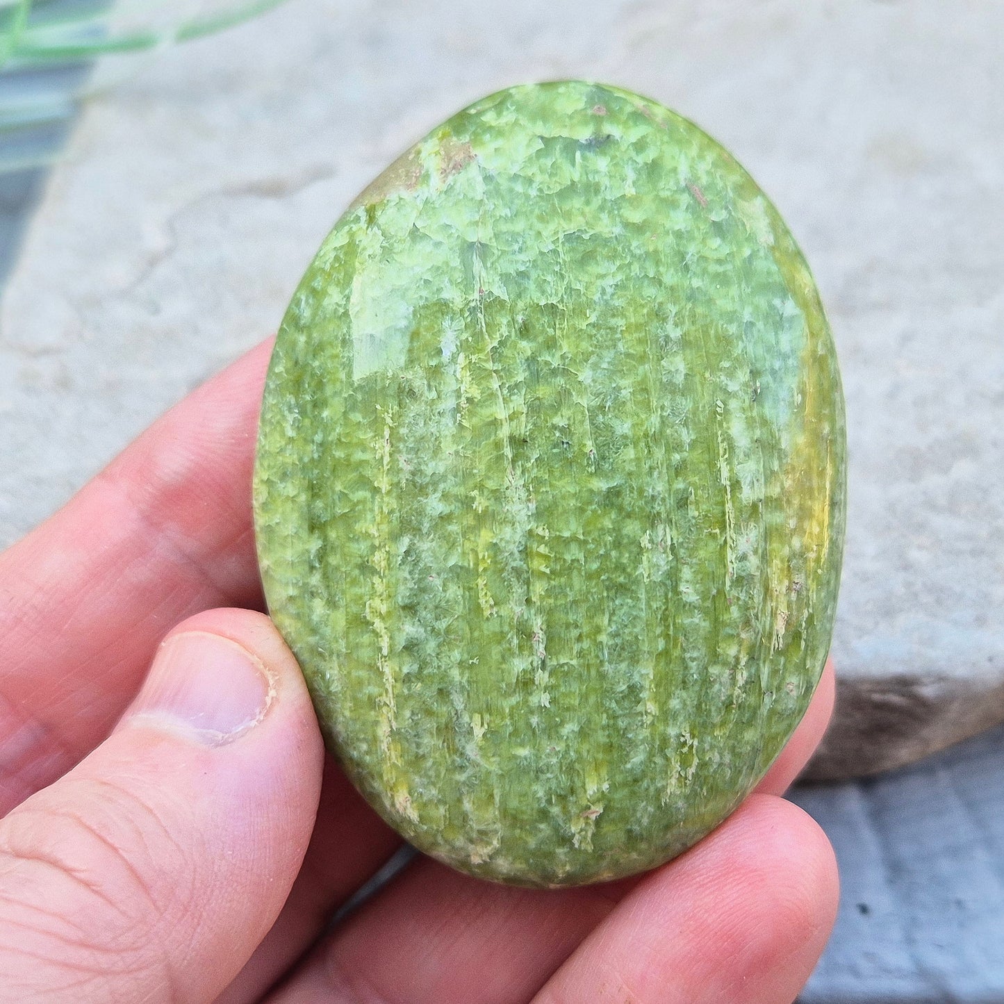 Tremolite Crystal Palm Stone. Lovely green colouring and smooth polished finish all over. Tremolite is a mineral found in the United States, formed when certain rocks like limestone are changed by heat and pressure. It comes in colors like white, grey, green, or light brown.