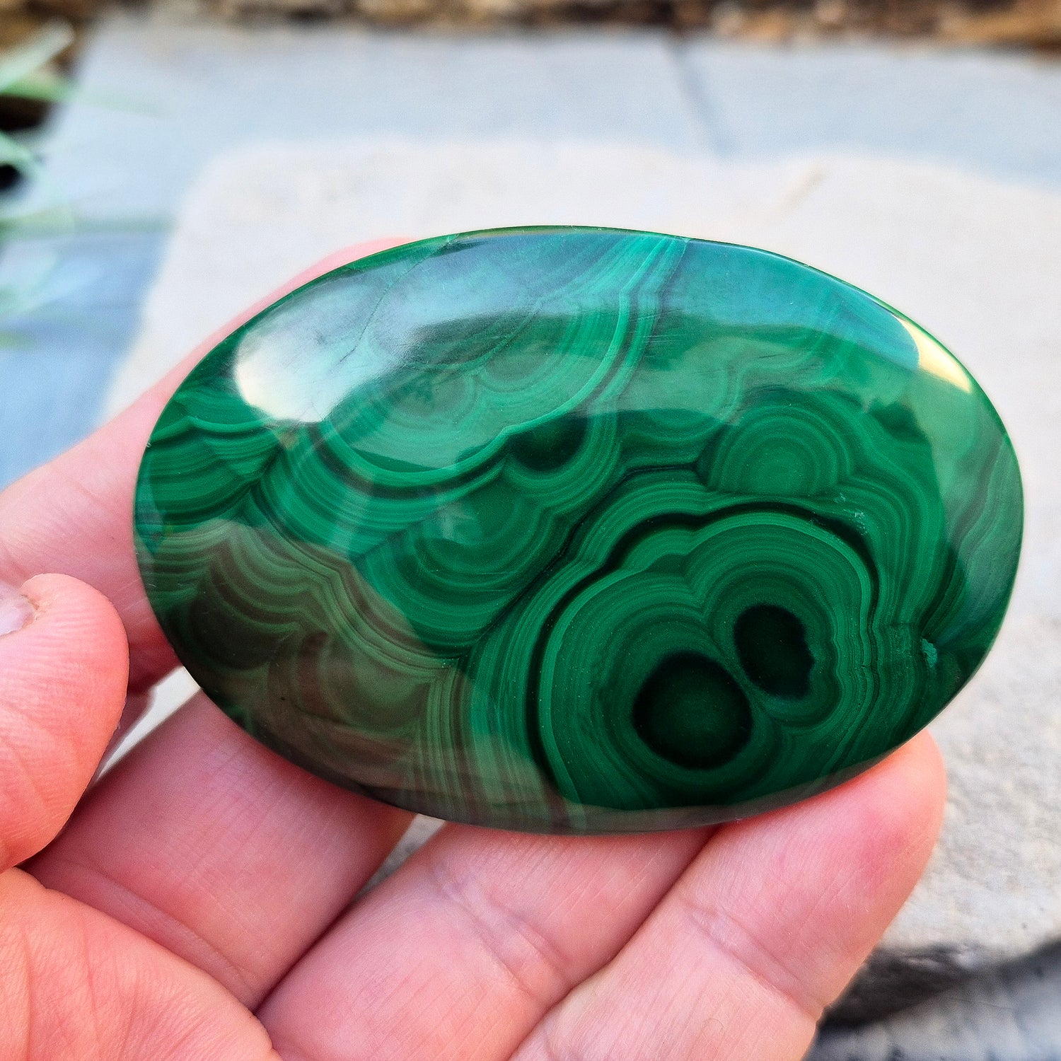 This stunning AA Grade Malachite palm stone features a rich blend of deep green hues and intricate banded patterns, polished for a comfortable feel in your hand.