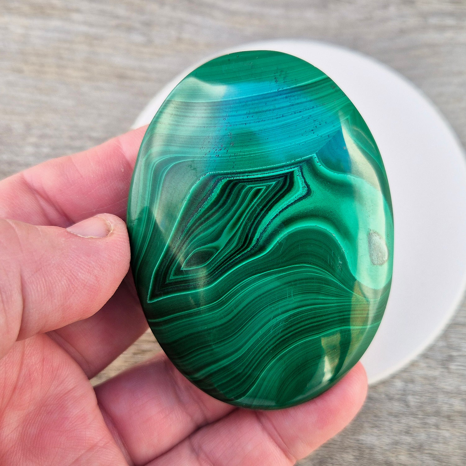 This stunning AA Grade Malachite palm stone features a rich blend of deep green hues and intricate banded patterns, polished for a comfortable feel in your hand. 