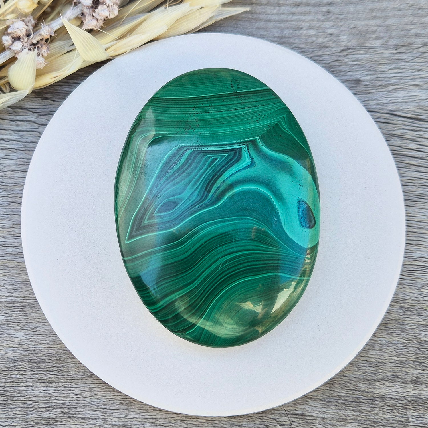 This stunning AA Grade Malachite palm stone features a rich blend of deep green hues and intricate banded patterns, polished for a comfortable feel in your hand. 
