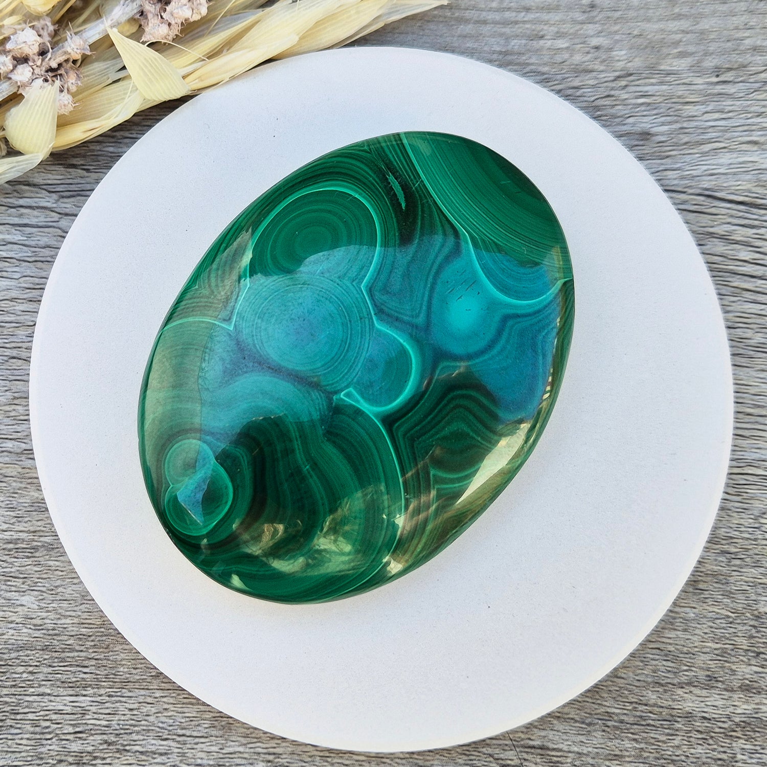 This stunning AA Grade Malachite palm stone features a rich blend of deep green hues and intricate banded patterns, polished for a comfortable feel in your hand. 