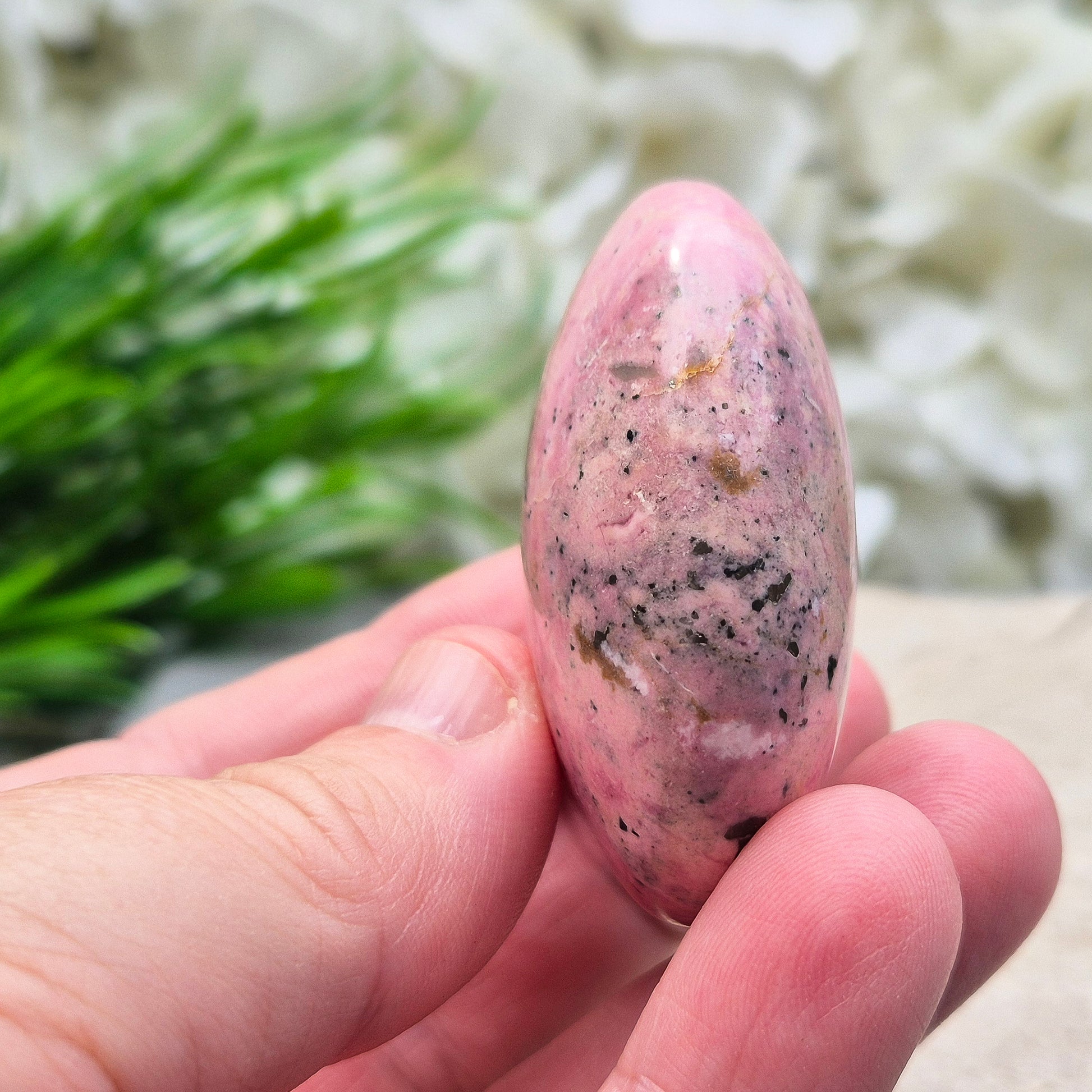 Pink Rhodonite Crystal Palm Stone – also known as Bubblegum Pink Rhodonite from Peru. This beautiful Rhodonite crystal, sometimes nicknamed Bubblegum Pink Rhodonite, comes from Peru and features a soft pink colour with black patches caused by the natural oxidation of manganese.