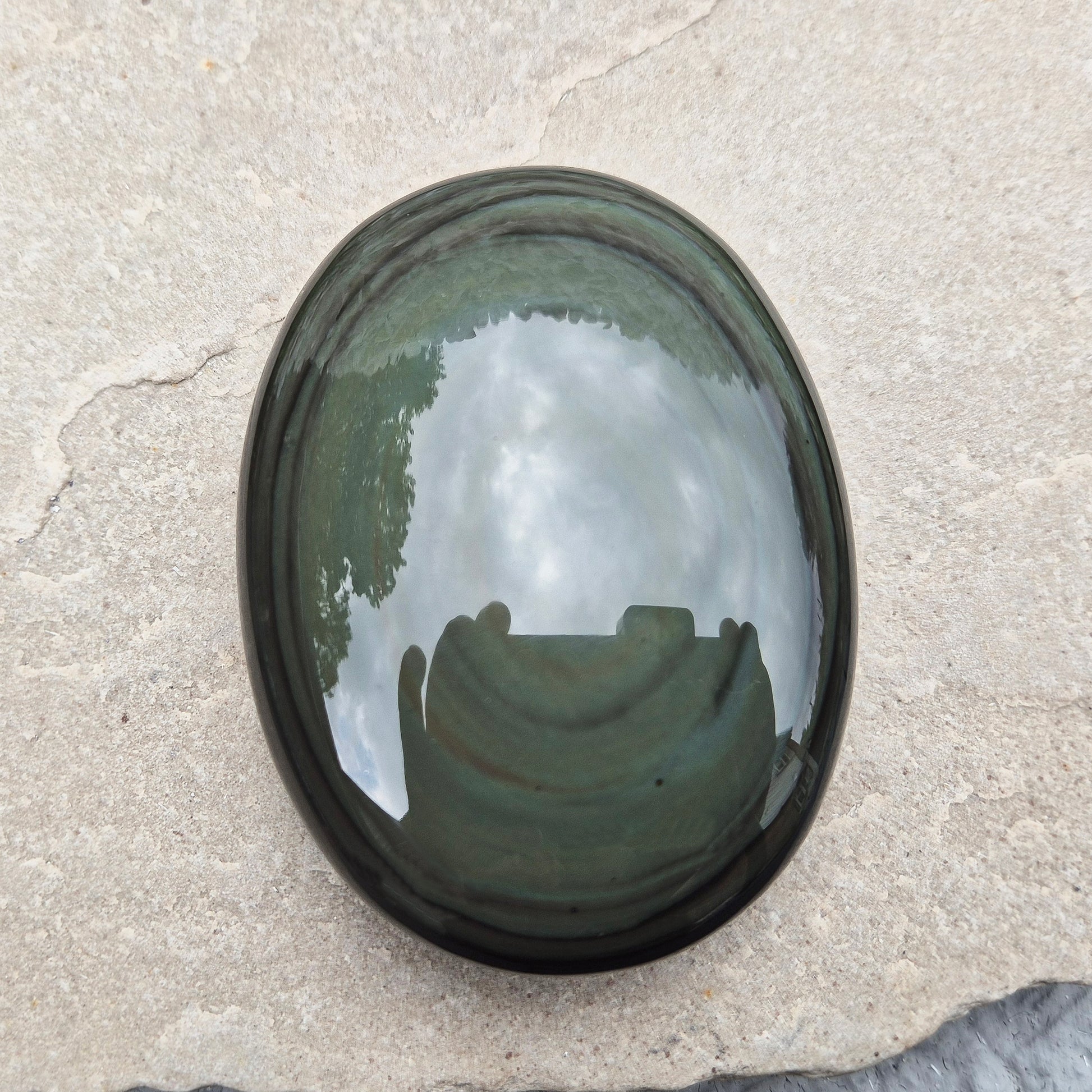 This highly polished, generously sized Rainbow Obsidian palmstone from Mexico reveals bands of deep green, gold, and shadowy blue — colours that only appear when the light hits just right.