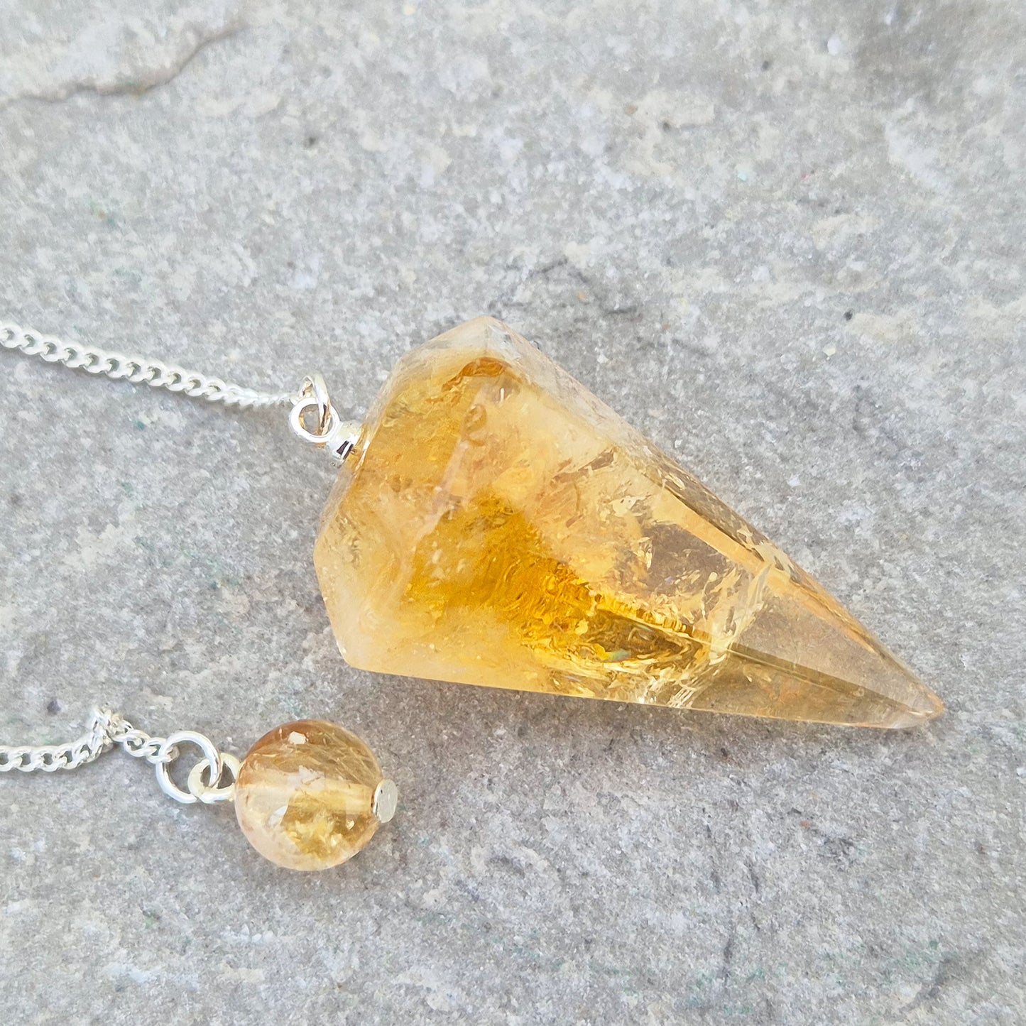 Citrine Crystal Pendulum from Brazil. This stunning sunny pendulum carrys the warm, golden glow Citrine is loved for. It has a yellow bead at the end of the chain making it comfortable to hold and easy to use.