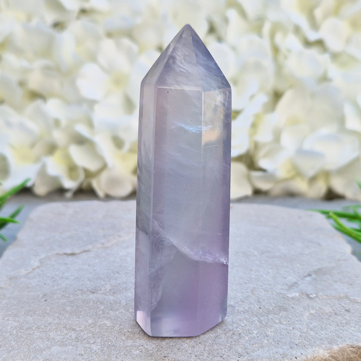 This Fluorite crystal point has a 6 faced generator tip, its pale lilac-grey body threaded through with soft smoky, feather-like inclusions and a faint blush of deeper pink pooling at the base