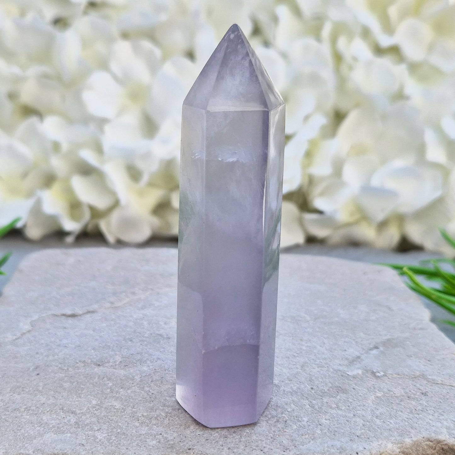This Fluorite crystal point has a 6 faced generator tip, its pale lilac-grey body threaded through with soft smoky, feather-like inclusions and a faint blush of deeper pink pooling at the base