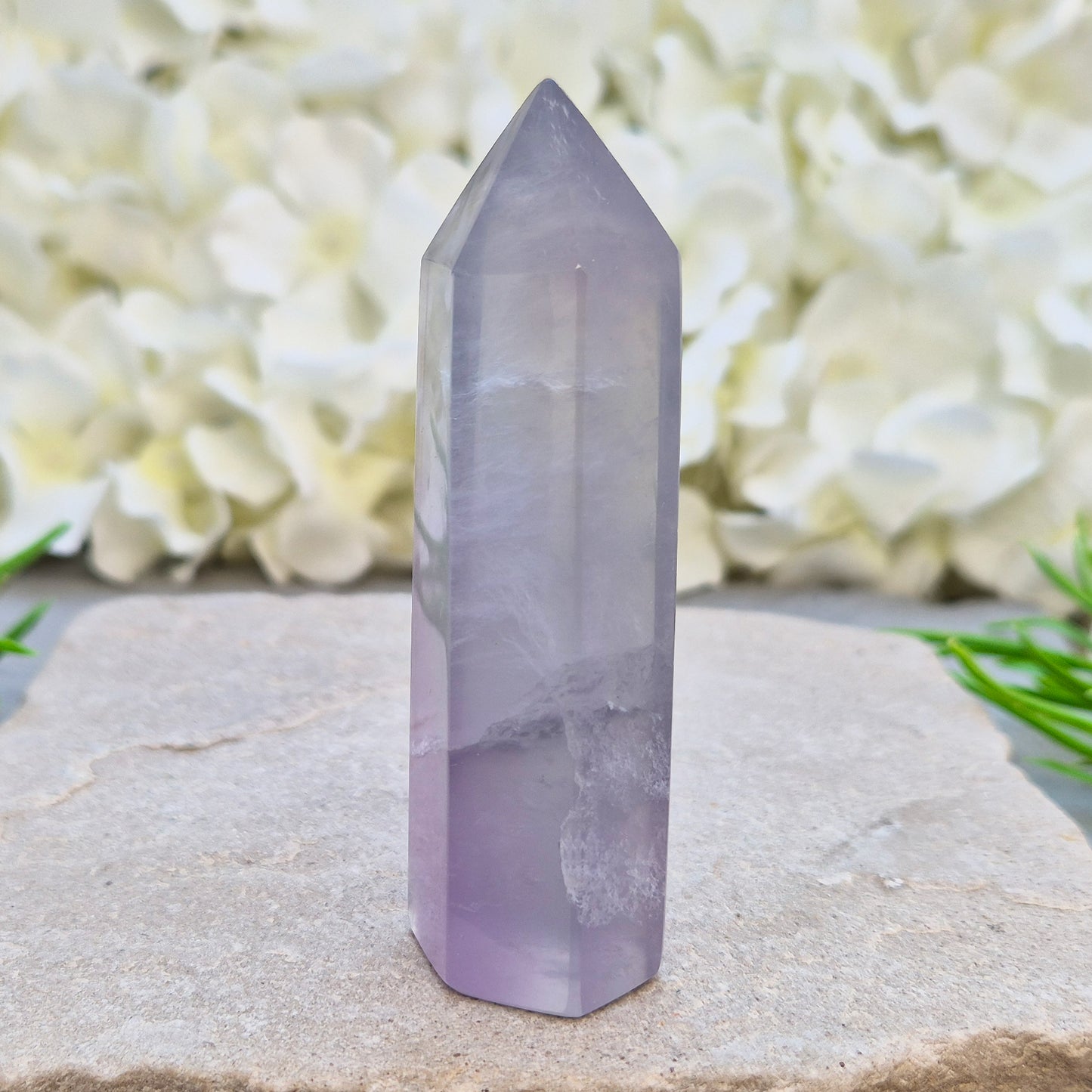 This Fluorite crystal point has a 6 faced generator tip, its pale lilac-grey body threaded through with soft smoky, feather-like inclusions and a faint blush of deeper pink pooling at the base