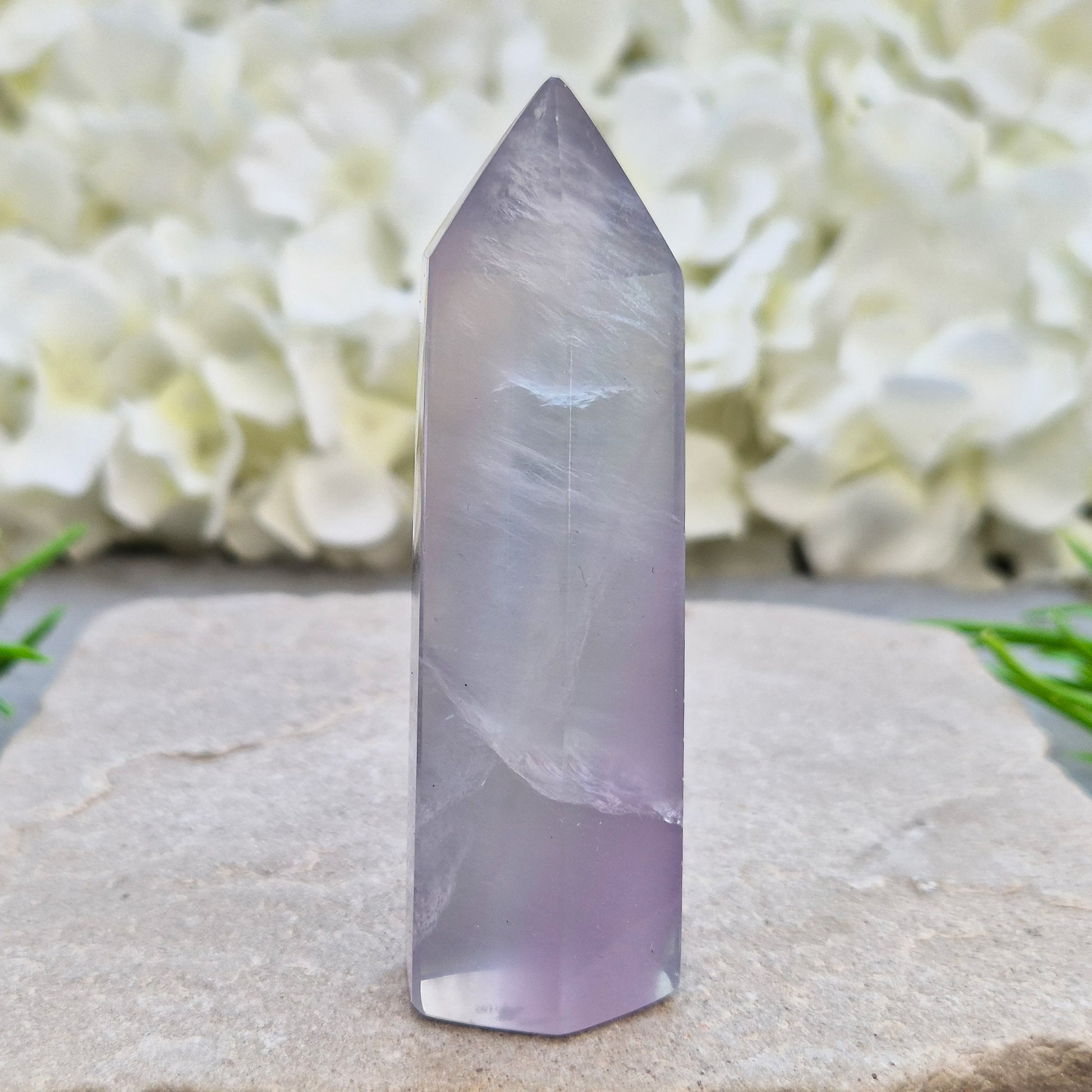 This Fluorite crystal point has a 6 faced generator tip, its pale lilac-grey body threaded through with soft smoky, feather-like inclusions and a faint blush of deeper pink pooling at the base
