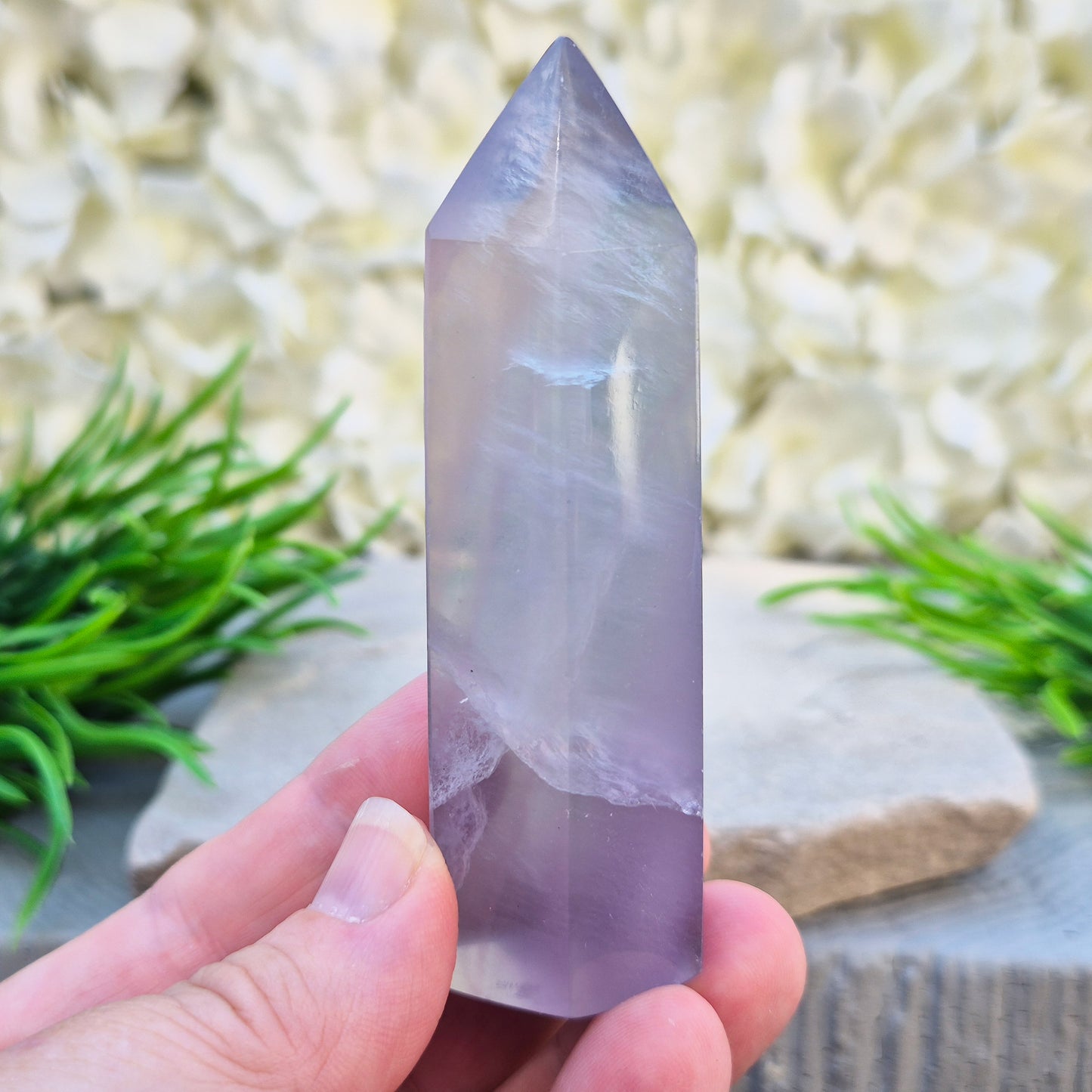 This Fluorite crystal point has a 6 faced generator tip, its pale lilac-grey body threaded through with soft smoky, feather-like inclusions and a faint blush of deeper pink pooling at the base