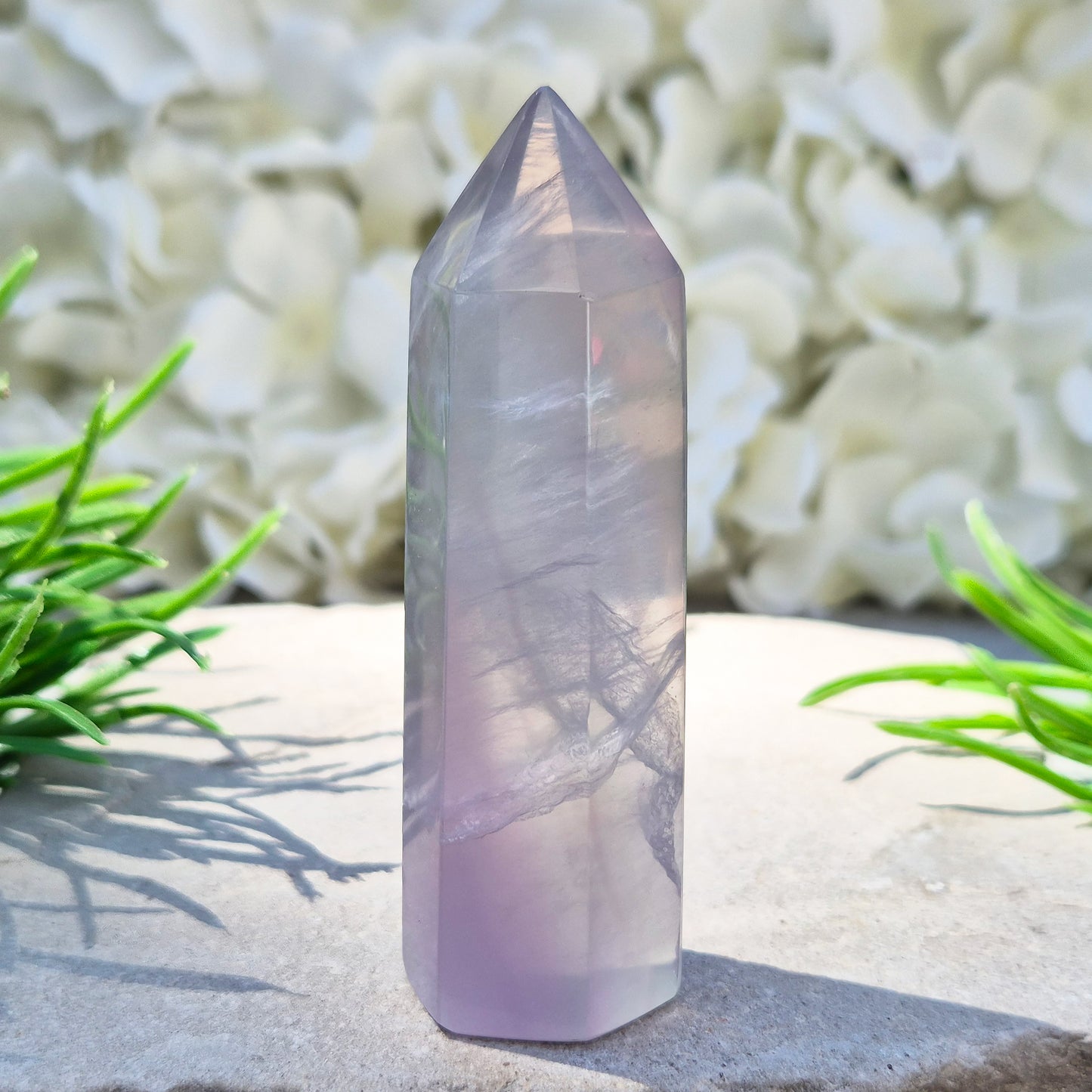 This Fluorite crystal point has a 6 faced generator tip, its pale lilac-grey body threaded through with soft smoky, feather-like inclusions and a faint blush of deeper pink pooling at the base