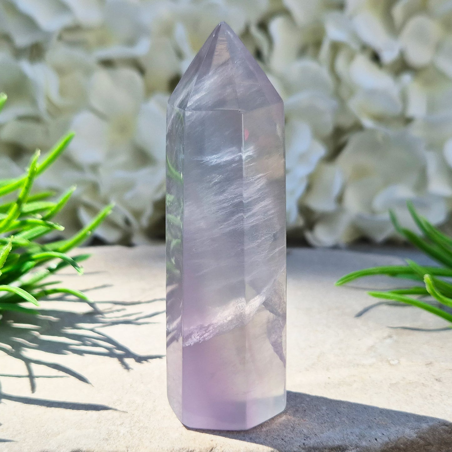 This Fluorite crystal point has a 6 faced generator tip, its pale lilac-grey body threaded through with soft smoky, feather-like inclusions and a faint blush of deeper pink pooling at the base