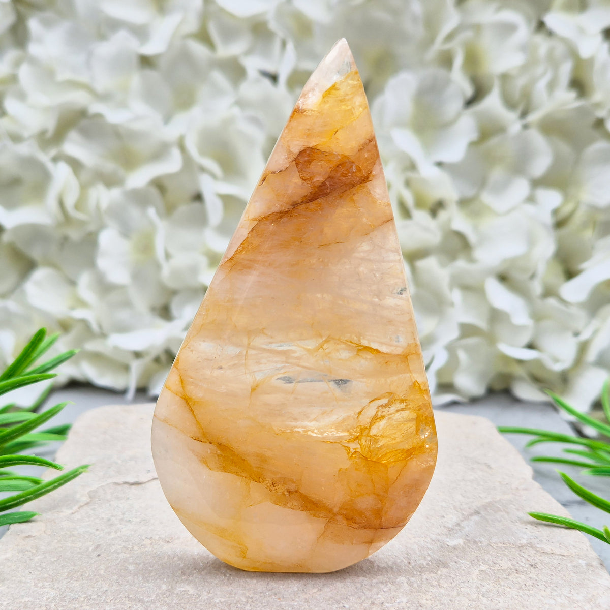 This Golden Healer Quartz teardrop is polished from Brazilian quartz, threaded through with golden inclusions of iron oxide inclusions (also known in the trade as yellow hematoid quartz). The smooth teardrop shape tapers to a clean point, standing upright on its own, with the golden banding visible right through the stone.