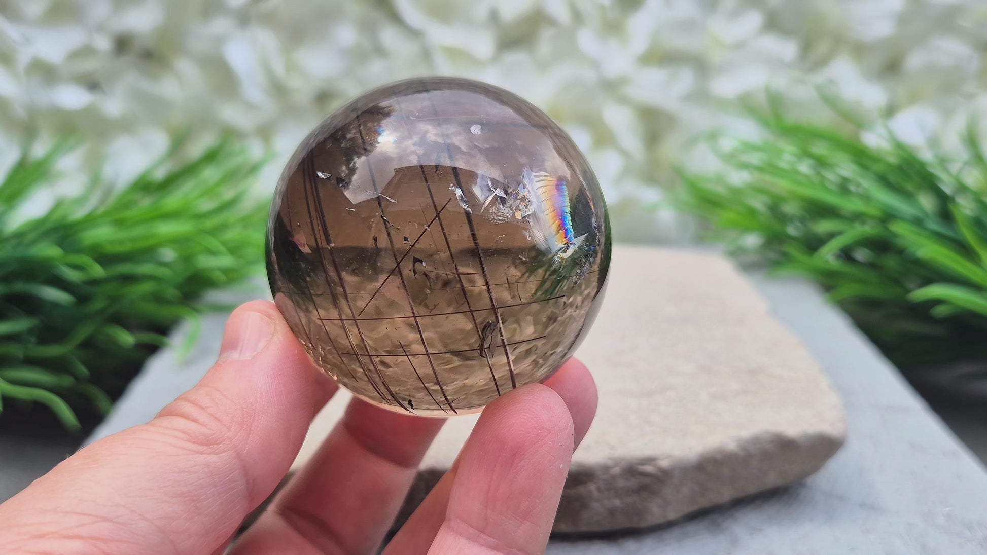 Smoky Quartz Sphere with Copper Red Rutile and rainbow flashes — grounding, protecting, and boosting creativity and clarity. Includes acrylic stand.